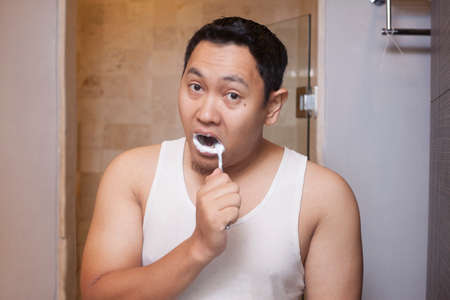 Portrait of attractive young Asian male brushing his teeth in bathroomの写真素材