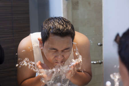 Portrait of attractive young Asian male wash his face in bathroomの写真素材