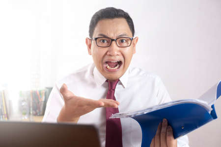 Portrait of Asian businessman boss manager tired sick stress to see bad report, yelling at his staff with angerの写真素材
