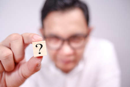 Close up image of businessman showing wooden block with question mark on it, selective focusの写真素材