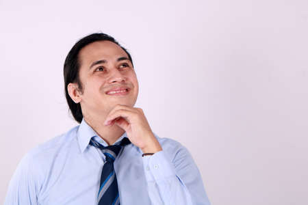 Photo image of young Asian man looked happy thinking and looking up, having good idea. Half body portrait against white wall with copy spaceの写真素材