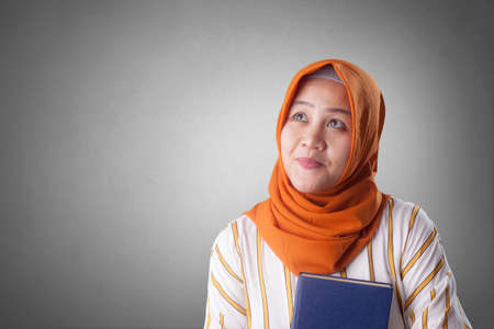Portrait of young muslim businesswoman wearing hijab holding book with thinking expressionの写真素材