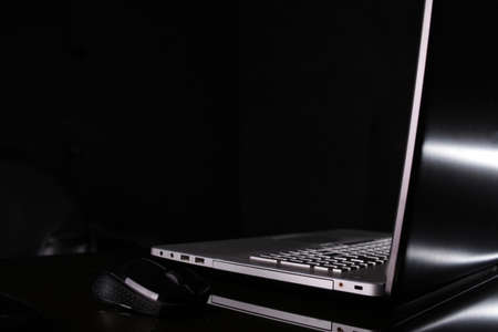 Silver laptop in the dark, black reflective surface and background with minimalist lighting,...