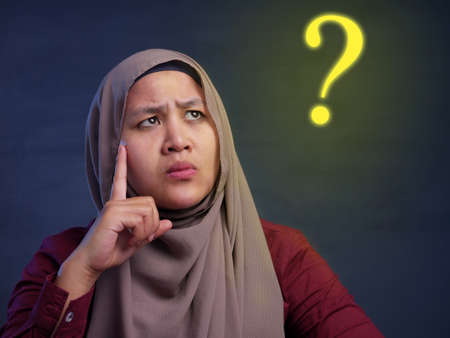 Asian muslim businesswoman wearing hijab with curiousity thinking expression and a question mark...