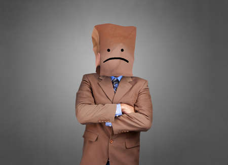 Portrait of businessman covering his face with paper mask with sad face drawn on it, bad negative sullen depression anonymouse personの写真素材