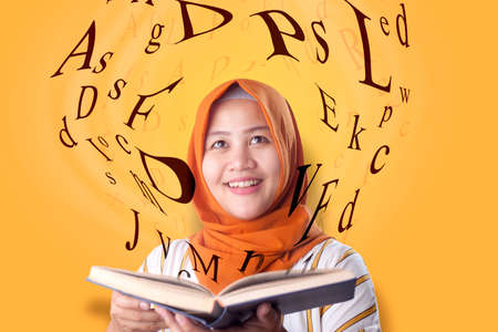 Portrait of beaautiful young Asian muslim woman smiling when reading book, magical book with letters...