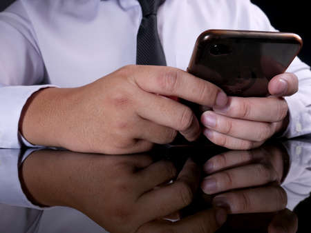 Close up image of businessman holding and using smart phone with dark black barground and reflective surface tableの写真素材