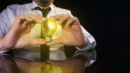 Businessman hold bulb lamp in his hand, shows new idea in business concept, against dark black backgroundの写真素材
