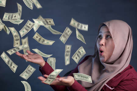 Portrait of happy successful young Asian billionaire muslim woman smiling happily under rain of money. Wealth investment economic conceptの写真素材