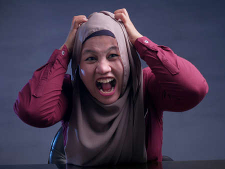 Portrait of angry stressed muslim businesswoman wearing hijab with mad insanity gestureの写真素材
