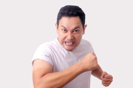 Photo image of funny Asian man showing cynical unhappy angry facial expression putting up his fist challenge to fightの写真素材