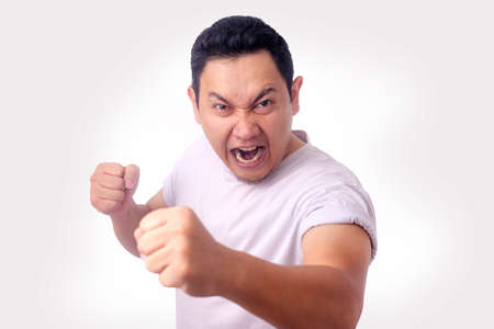 Photo image of funny Asian man showing cynical unhappy angry facial expression putting up his fist...