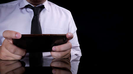Close up image of businessman holding and using smart phone with dark black barground and reflective...