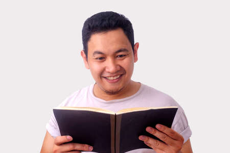 Portrait of Asian man wearing casual white shirt looked happy and smiling while reading a bookの写真素材
