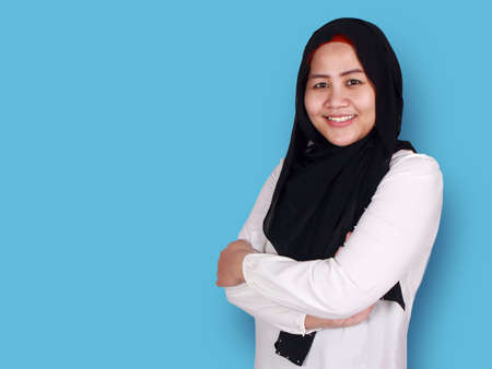 Asian muslim businesswoman wearing hijab smiling friendly with arms crossed, young woman standing...