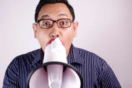 Photo image portrait of funny young Asian man shouting with megaphone, mad yelling screaming crazy supporting motivating conceptの写真素材