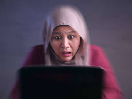 Portrait of muslim businesswoman wearing hijab shocked stunned when looking at laptop, bad negative...
