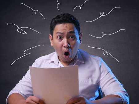 Portrait of funny Asian businessman shocked surprised with open mouth to see financial report, bad...