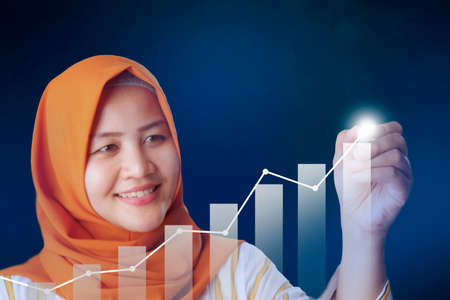 Asian muslim businesswoman drawing business target diagram, performance indicator in virtual screeen, stock market infographicの写真素材