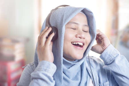 Portrait of young beautiful Asian muslim woman wearing hijab listening music with a headphonesの写真素材
