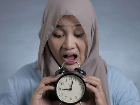 Young Asian businesswoman wearing suit and hijab worried by time when looking at a clock. Close up body portraitの写真素材