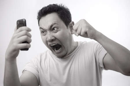 Attractive young Asian man talking on his phone, getting bad news, shocked mad angry gestureの写真素材