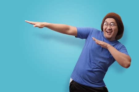 Portrait of funny Asian man smiling and making dab movement, against blue background
