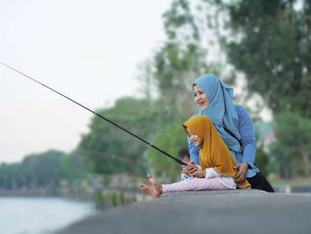 Portrait of happy muslim mother and her little baby daughter having fun outdoor, fishing leisure activity on summer dayの写真素材
