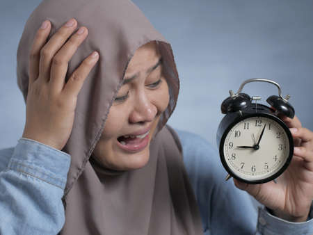 Young Asian businesswoman wearing suit and hijab worried by time when looking at a clock. Close up body portraitの写真素材