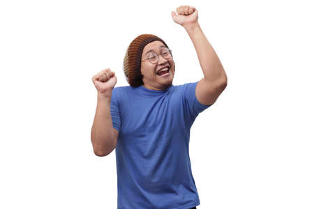 Portrait of a funny young Asian man wearing blue shirt dancing happily joyful expressing celebrating good news victory winning success gesture, smiling positive excited emotion isolated on whiteの写真素材