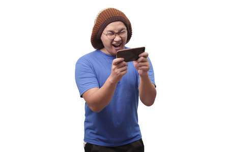 Photo image portrait of a cute handsome young Asian man with funny face playing games on tablet...