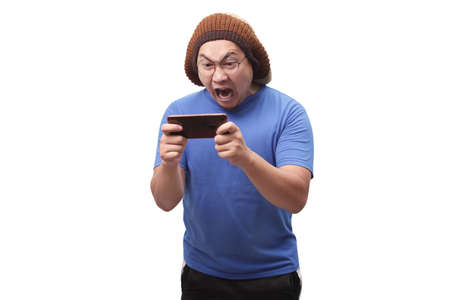 Portrait of a cute handsome young Asian man with funny face playing games on tablet, sad angry...
