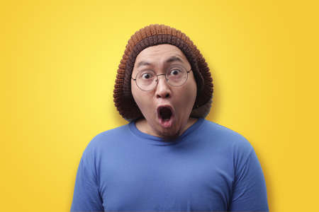 Portrait of young funny Asian man shocked or surprised expression with mouth open, against yellow backgroundの写真素材