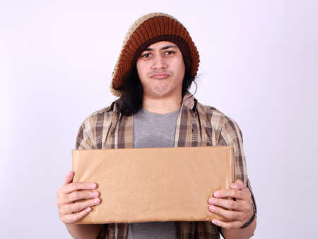 Portrait of young good looking Asian courier delivery man giving box of parcel package, looking at camera amd smiling, isolated on whiteの写真素材