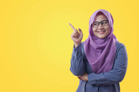 Asian muslim businesswomen wearing hijab with curiousity thinking expression. Having good idea, against yellow backgroundの写真素材
