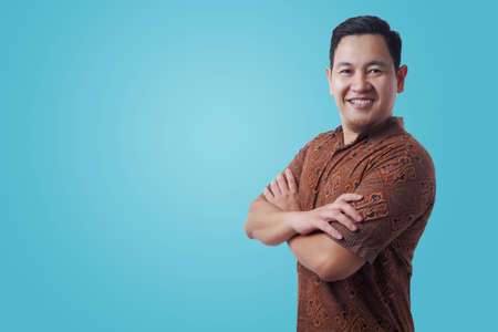 Portrait of happy successful Asian man wearing batik shirt smiling confidently wit arms crossed on...