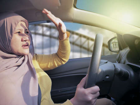 Portrait of Asian muslim female driver get blinded, disturbed dazzled by sun lightの写真素材