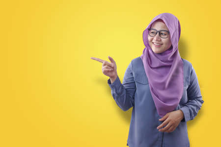 Portrait of attractive beautiful muslim woman wearing hijab  smiling and pointing to the side with...