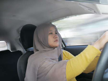 Portrait of young Asian muslim woman smiling and driving a car, good looking entrepreneur, car sharing conceptの写真素材