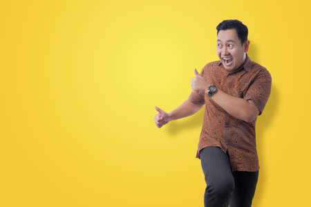 Happy funny young Asian man wearing Indonesian batik shirt dancing happily joyful expressing...