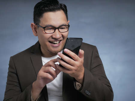 Attractive young Asian man reading texting chatting on his phone, smiling happy laughing expressionの写真素材