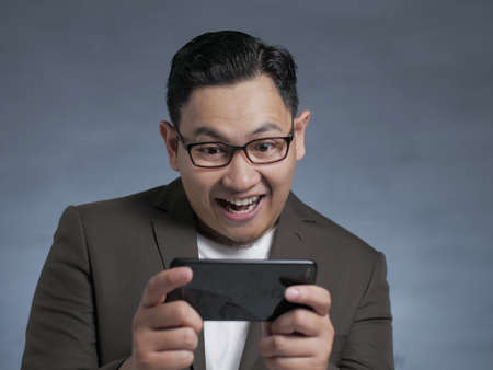 Portrait of a cute handsome young Asian businessman playing games on tablet smart phone