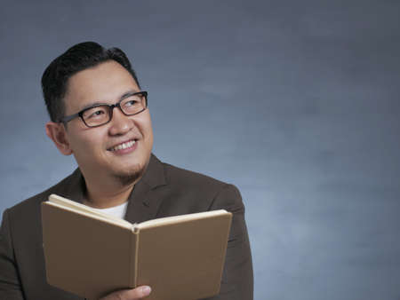 Young smart Asian man holding a book with thinking expression, book source of knowledge concpet