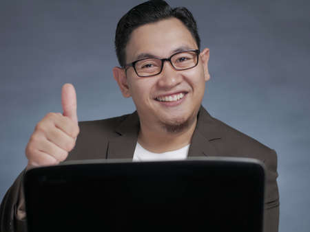 Young Asian businessman working typing on his laptop, smiling expression. Close up body portrait
