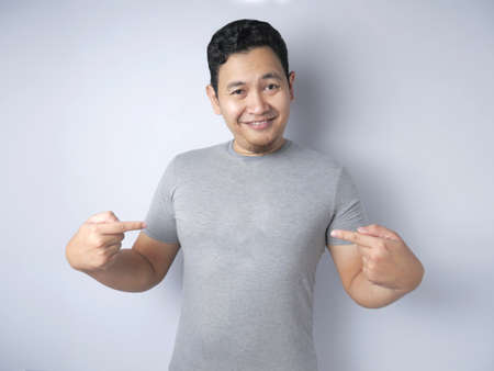 Funny happy Asian man smiling and pointing himself, confidence concept, close up portrtait against...