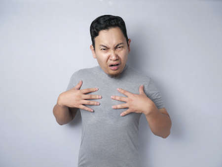 Asian man pointing himself with unhappy displeased expression as if he confused to be accused and...