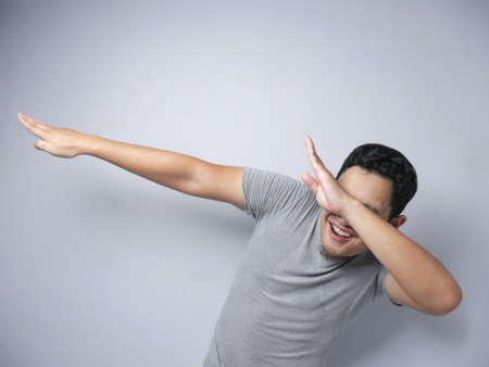 Portrait of funny Asian man smiling and making dab movement, over gray backgroundの写真素材