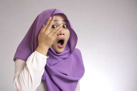 Portrait of Asian muslim woman worried, shocked and peeking through her fingersの写真素材