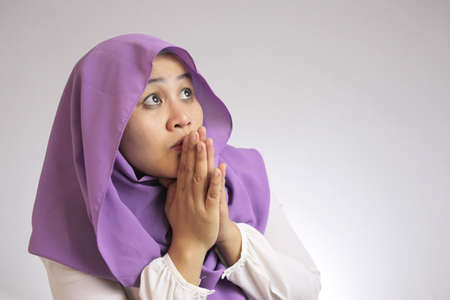 Portrait of young Asian muslim woman looks worried and nervous looking up to the side, afraid of something badの写真素材