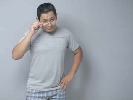 Portrait of young Asian man looking at camera, smiling and adjusting eyeglasses, checking his sight problem, over grey backgroundの写真素材